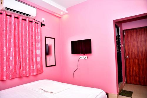 卡兰古特INDRAYANI GUEST HOUSE的粉红色的卧室配有床和电视