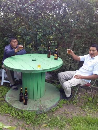 基多Hospedaje el Motilon的两个男人坐在一张绿桌旁,喝着啤酒