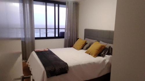 蒙得维的亚Modern apartment first line beach Montevideo UY的一间卧室配有一张带黄色枕头的床和一扇窗户