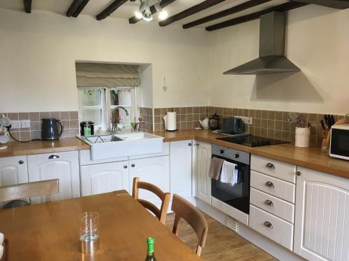 拉尼德洛伊斯200 year old Gardener's cottage, Mid Wales的厨房配有白色橱柜和木桌