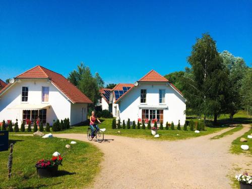 VerchenHoliday Home Ferienpark Verchen-2 by Interhome的一位妇女骑着自行车在两座白色房子前