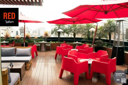 利马Radisson RED Miraflores的一间设有红色椅子、桌子和遮阳伞的餐厅