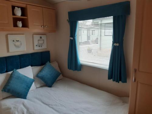 Gilcrux24 The Beeches Caravan Park的一间卧室配有一张带蓝色窗帘的床和一扇窗户
