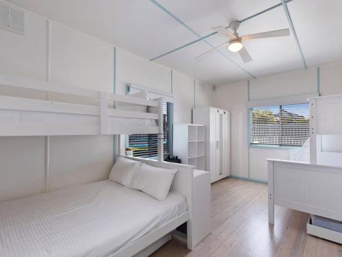 Long JettyPacific Family Retreat的卧室配有白色双层床和吊扇