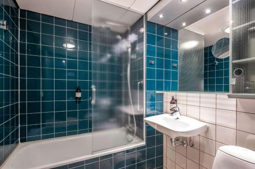 欧登塞Comwell H C Andersen Dolce by Wyndham的浴室铺有蓝色瓷砖,配有水槽和淋浴。