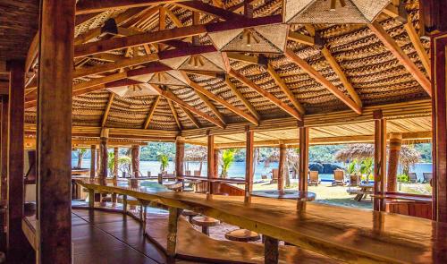 KuataBarefoot Kuata Island Resort的一个带木桌和长椅的大型木制凉亭