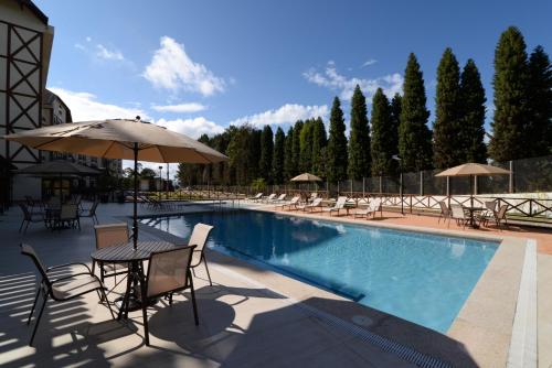 AracêVista Azul Apart Hotel - Vista Pinheiros的一个带桌椅和遮阳伞的游泳池