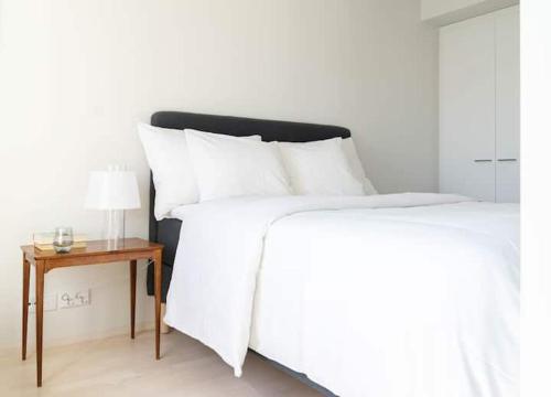 赫尔辛基Stylish new 1br apt in Aurinkolahti的一张带白色床单的床和一张带台灯的桌子