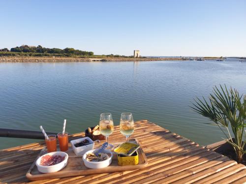 马格隆新城Peniche Alphonsia Maria的湖上一张桌子,上面放着两杯葡萄酒和食物