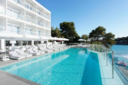 波蒂纳茨Grupotel Ibiza Beach Resort - Adults Only的一座带白色椅子的游泳池和一座建筑