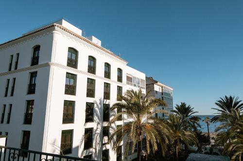 EsteponaHotel Estepona Plaza的一座白色的建筑,在海洋前方种有棕榈树