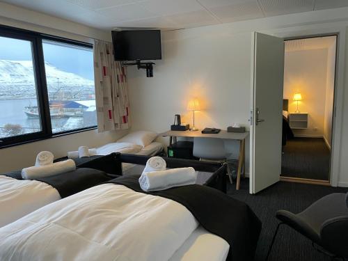 RunevigHotel Runavík的酒店客房设有三张床、一张书桌和一个窗户。