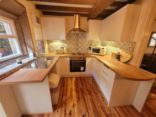 HeptonstallHeptonstall Cottage, Heptonstall, Hebden Bridge的厨房铺有木地板,配有白色橱柜。