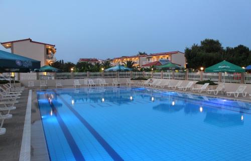 阿尔库季岛Ionion Beach Apartment Hotel & Spa的一座带椅子和遮阳伞的大型游泳池(晚上开放)