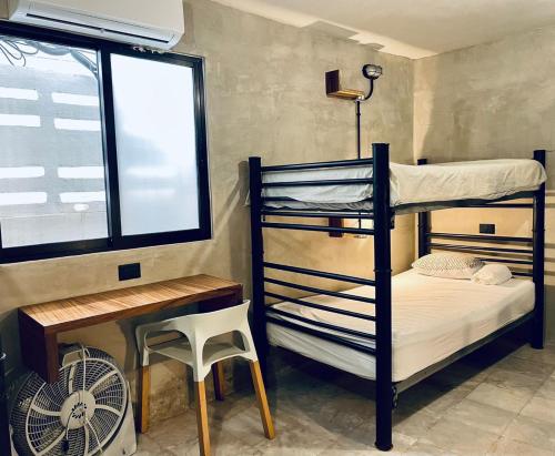 坎昆Moloch Hostel & Suites的一间卧室配有双层床、一张桌子和一个窗户。