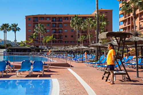 福恩吉罗拉福恩吉罗拉米拉马尔公寓式酒店的站在游泳池旁的男人,手持椅子和遮阳伞