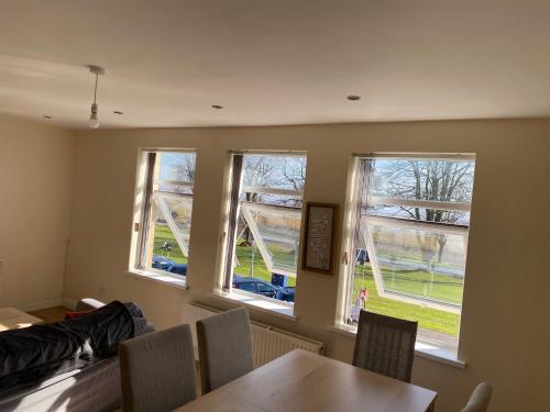 斯旺西Sea-view flat near Mumbles.的一间设有三扇窗户和一张桌子及椅子的用餐室