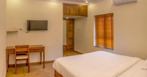 特里凡得琅Ekana Homes的一间卧室配有一张床、一张书桌和一台电视