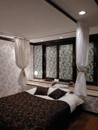 岸和田市ホテルサバナリゾートＡｄｕｌｔ Ｏｎｌｙ的一间卧室配有床和两个带窗帘的窗户