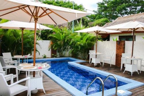 塞隆贝拉纳克Burudika Bungalows的一个带桌子和遮阳伞的庭院和一个游泳池