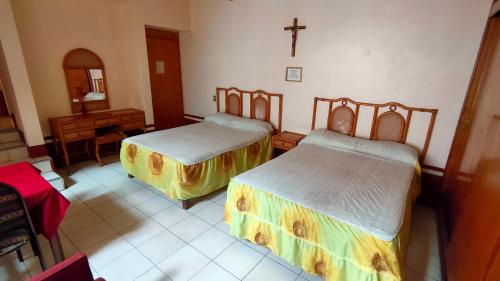 赫雷斯加西亚萨利纳斯OYO Posada Santa Cecilia, Jerez Zacatecas的一间设有两张床的客房,墙上有一个十字架