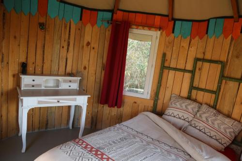 VillelaureLA HUTTE MASSAÏ的一间卧室配有一张床、一张书桌和一个窗户。