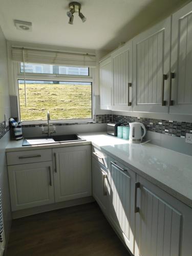 达特茅斯238 Norton Park, Dartmouth 2 bed holiday home with free parking的厨房配有白色橱柜、水槽和窗户。