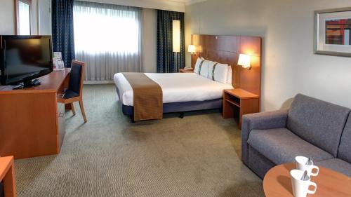 梅德斯通假日梅德斯通-七橡树酒店的酒店客房配有床、沙发和电视。