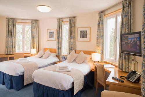 剑桥马丁利礼堂旅舍的配有书桌和电视的客房内的两张床