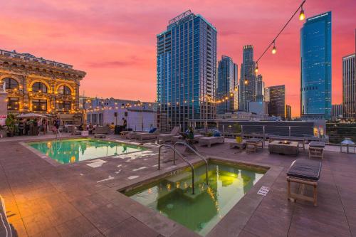 洛杉矶One Lux Stay HWH Downtown Los Angeles的屋顶游泳池,在日落时分享有城市天际线