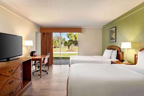 代托纳海滩Baymont by Wyndham Daytona Beach - Intl Speedway的酒店客房设有两张床、一张桌子和一台电视。