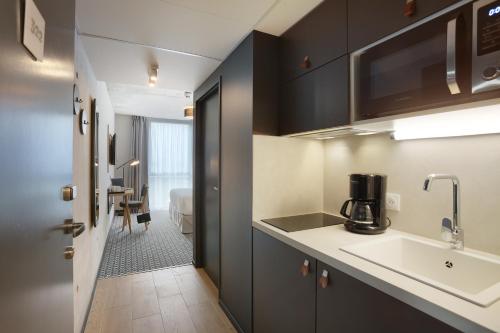布拉尼亚克Odalys City Toulouse Blagnac Aéroport的一间厨房,配有黑色橱柜和水槽,还有一间房间