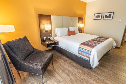 克萨尔特南戈LATAM HOTEL Plaza Pradera Quetzaltenango的配有一张床和一把椅子的酒店客房