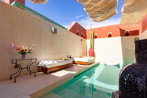 马拉喀什无忧宫卡伊兹摩洛哥传统庭院（住宅）的一座带两张床和一张桌子的游泳池,位于大楼旁