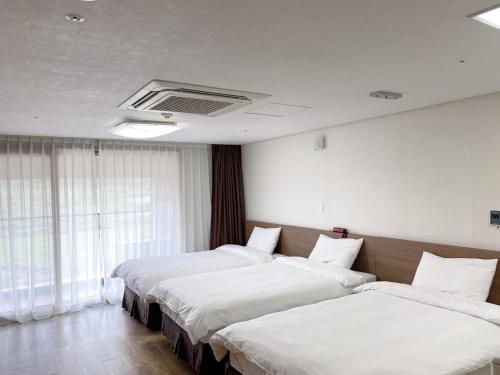 济州市Hi Jeju Hotel的配有白色床单的酒店客房内的两张床