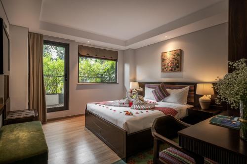 胡志明市奥莱传奇酒店的一间卧室配有一张床、一张书桌和两个窗户。