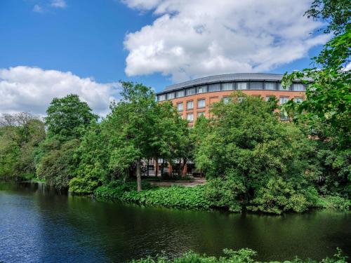 不莱梅Dorint City-Hotel Bremen的河岸边的一座有树木的建筑