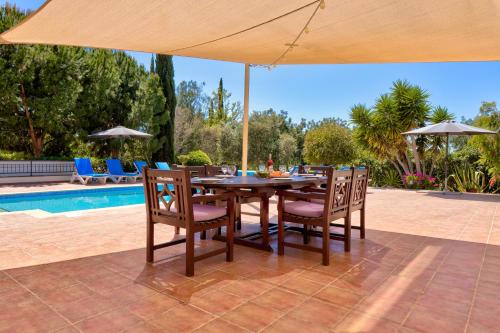 库克里亚4 bedroom Villa Kellia with private pool, Aphrodite Hills Resort的一张带椅子的木桌和一把遮阳伞,毗邻游泳池