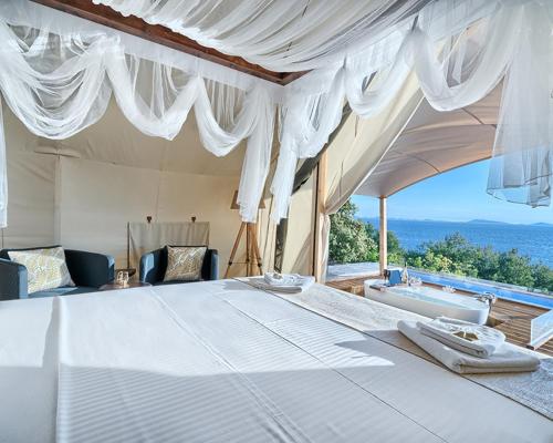 穆泰尔岛Golden Haven Luxe Glamp Resort的卧室配有一张白色大床和浴缸