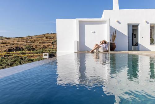 圣罗曼诺斯Kapsalos Villas的坐在房子旁边的游泳池旁的女人