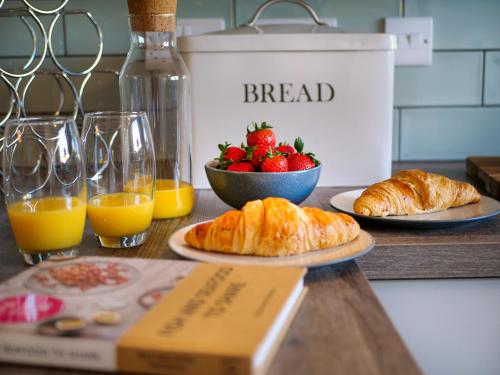 圣梅尔林Padstow Escapes - Breakers Holiday Cottage的桌子,上面有面包和一碗草莓和橙汁