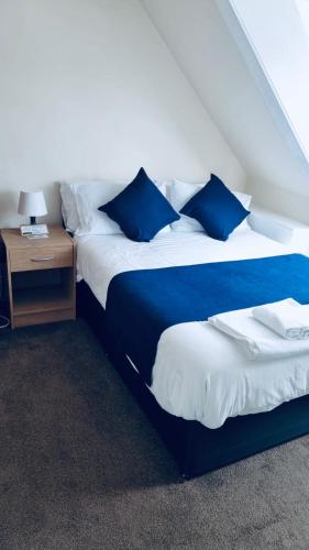 威克Caithness Inn的一间卧室配有两张带蓝色枕头和桌子的床