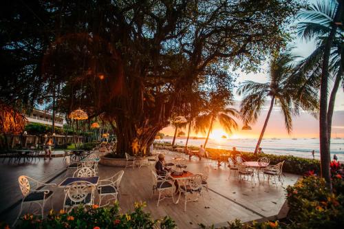 塔马林多Hotel Tamarindo Diria Beach Resort的日落时在海滩上摆放着几张桌子和椅子