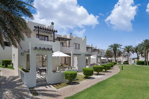 艾恩Radisson Blu Hotel & Resort, Al Ain的一座白色的大建筑,有树木和草地