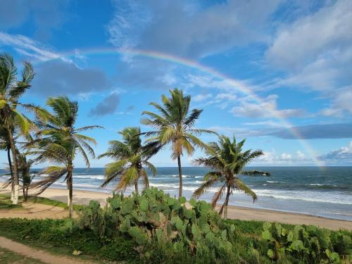 萨尔瓦多Casa (Village) beira mar em Praia do Flamengo的棕榈树和海洋海滩上的彩虹