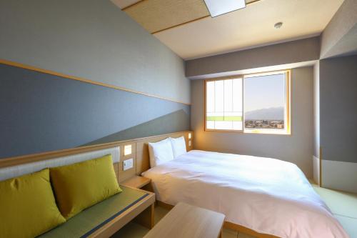 松本Onyado Nono Matsumoto Natural Hot Spring的一间卧室配有一张床、一张长凳和一个窗户。