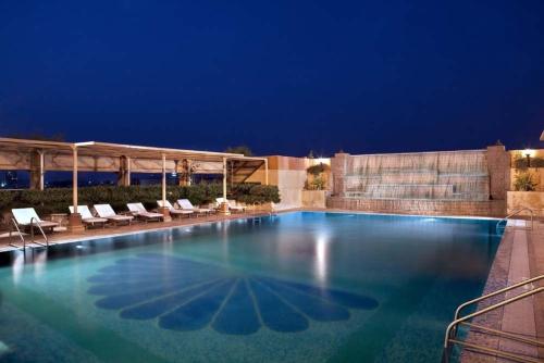 古尔冈布里斯托尔酒店的夜间大型游泳池,配有躺椅