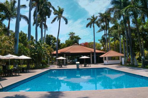 库利亚坎InHouse Select Hacienda Tres Rios的一座拥有棕榈树、桌子和遮阳伞的游泳池
