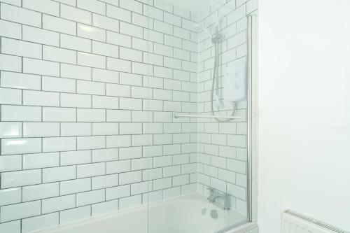 特伦特河畔伯顿Heath House的白色瓷砖浴室设有淋浴和浴缸。