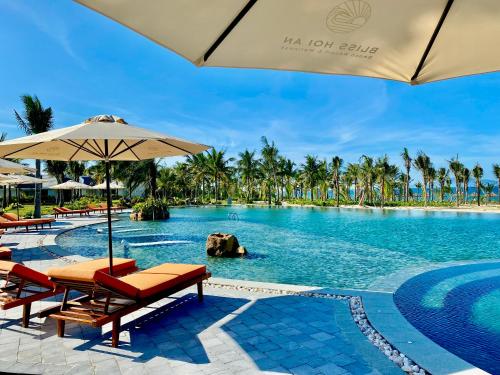 会安Bliss Hoi An Beach Resort & Wellness的一个带椅子和遮阳伞的度假村游泳池